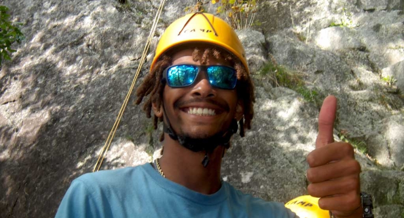 A person wearing a helmet smiles at the camera and gives a thumbs up